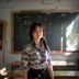 小学语文老师李晓梅的照片，扎马尾的年轻女教师站在教室黑板前，阳光从窗户照进来